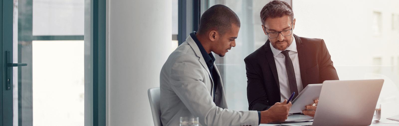 Two individuals in a modern office setting discussing work with a tablet.