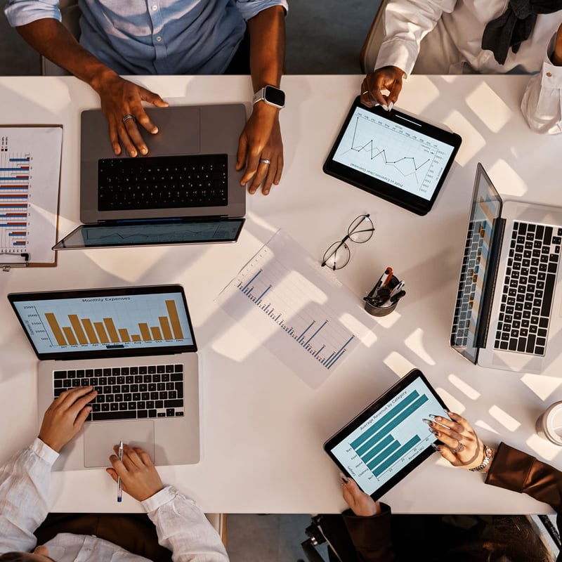 coworkers sitting at conference room table meeting and working on computers with data graphs